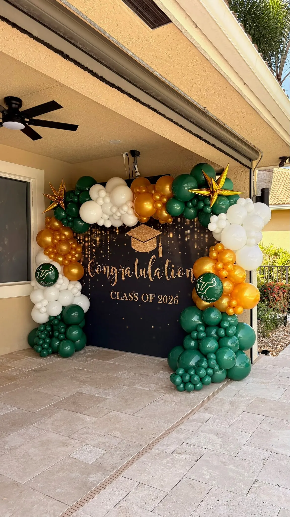 Green, gold and white balloon garland with gold starbursts framing a black graduation backdrop