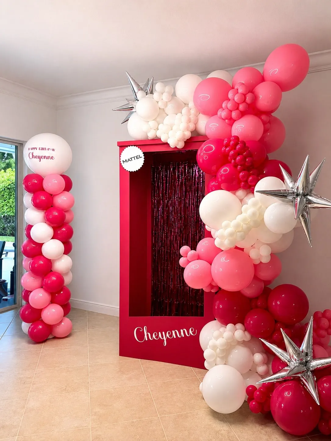 Hot pink and white balloon garland with silver stars on a life-size doll box frame, with a balloon column beside it