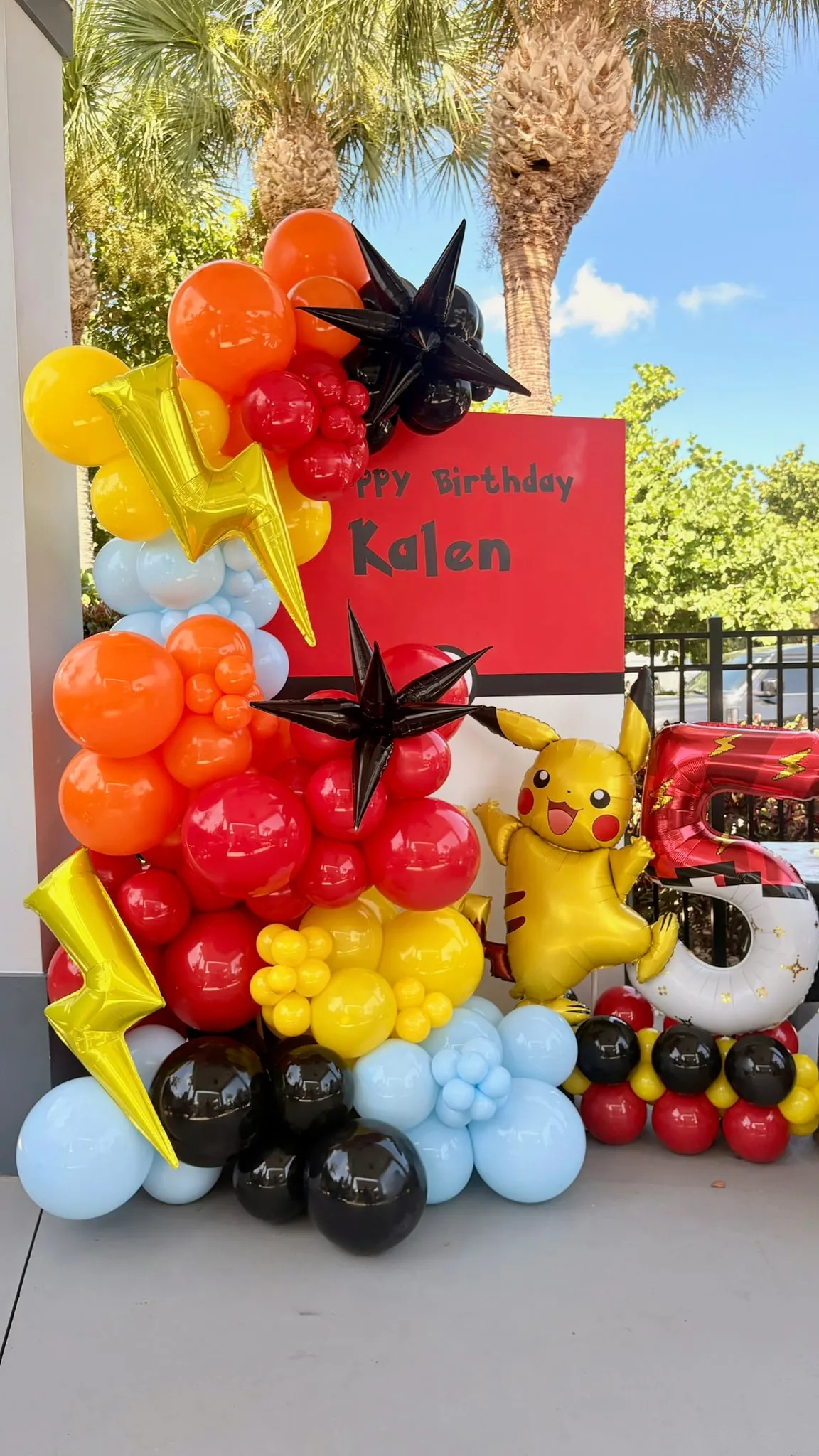 Tall balloon garland in red, orange, yellow, blue and black with gold lightning bolts beside a birthday sign