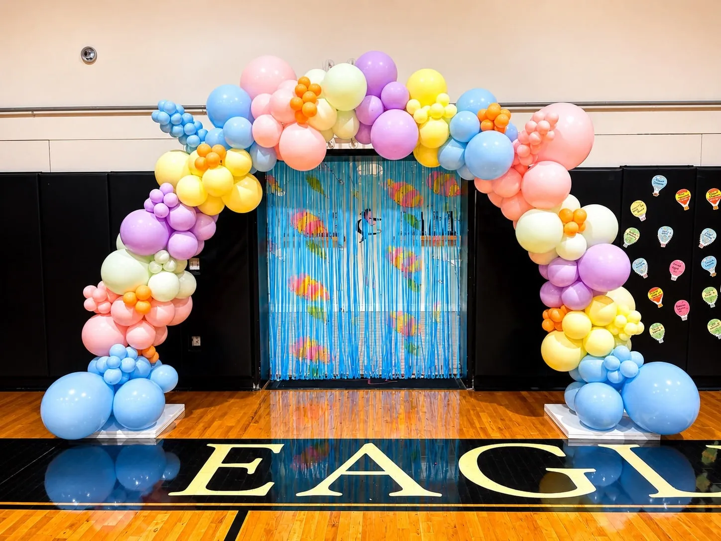 Pastel rainbow balloon arch standing on a polished gym floor