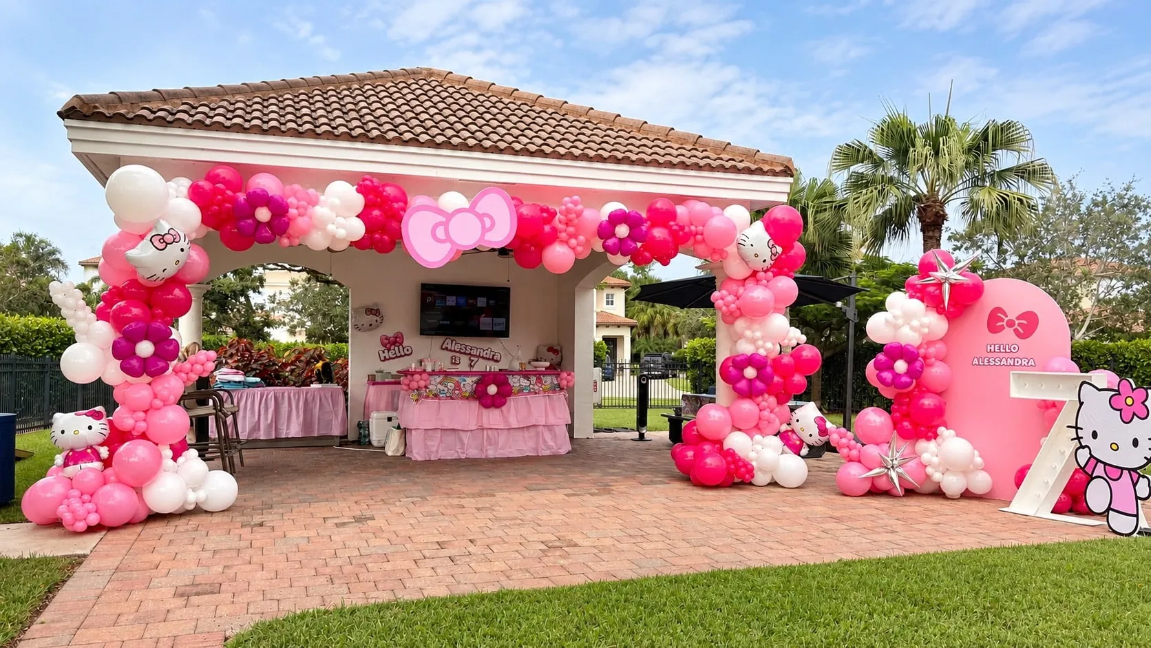 Outdoor pavilion framed with pink and white balloon garlands, with a pink backdrop to one side