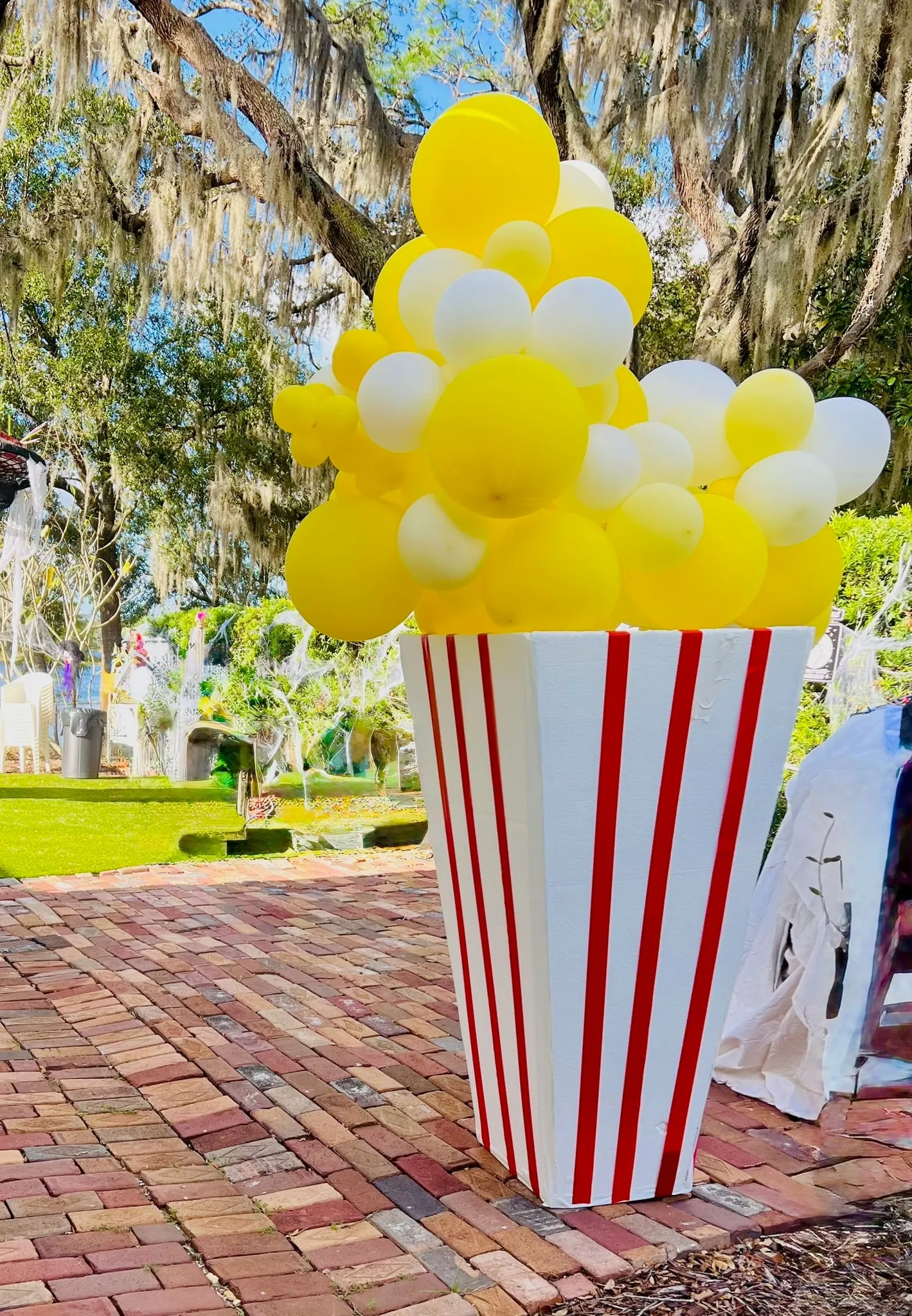 Large red and white striped popcorn box filled with yellow and white balloons