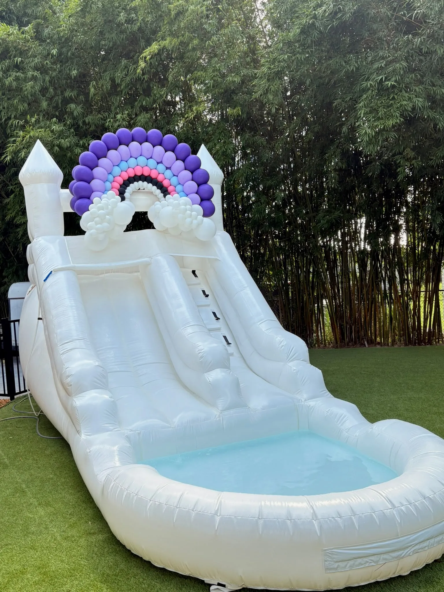 Balloon rainbow in purple, pink and white on top of a white inflatable slide