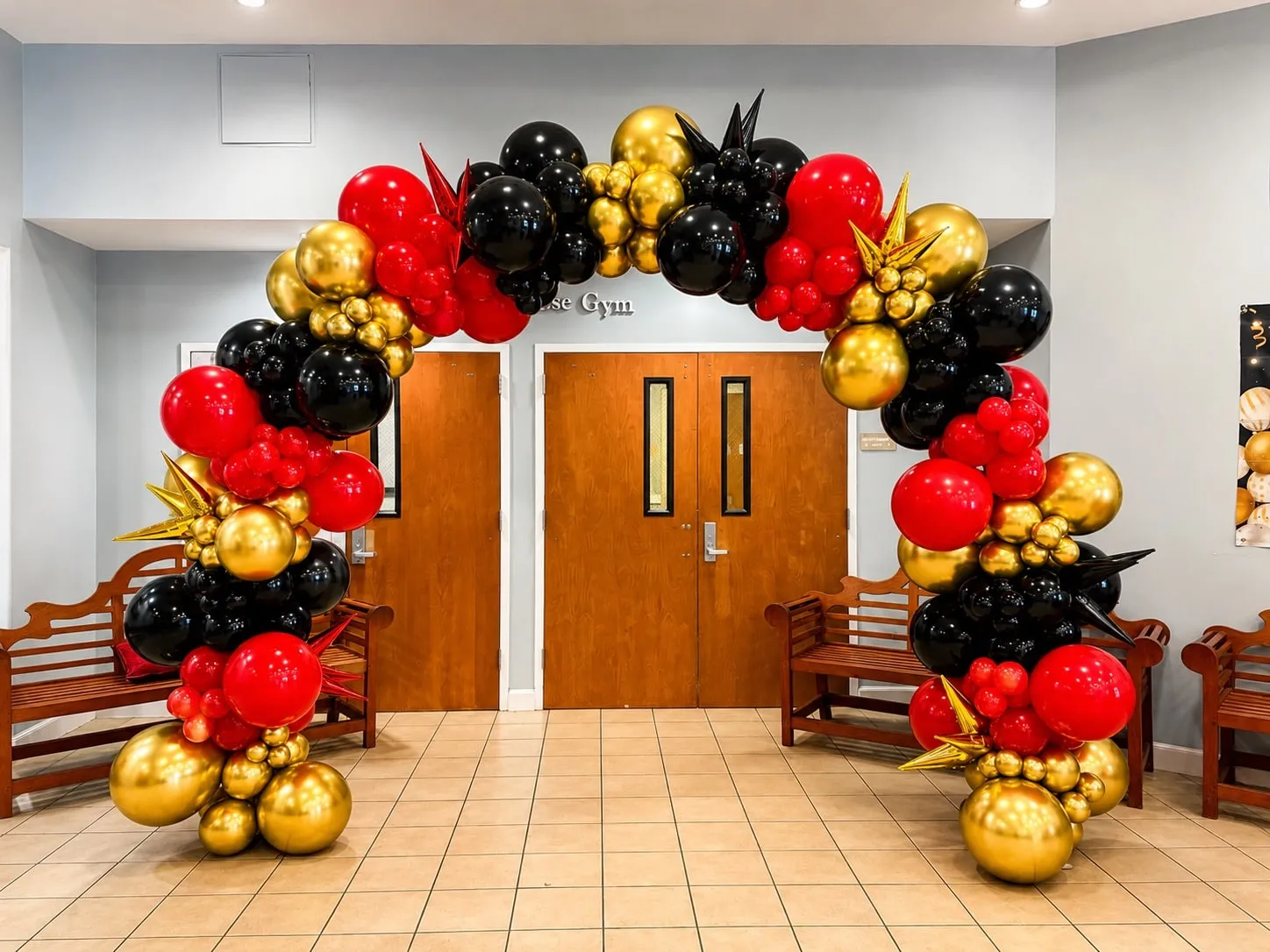 Red, black and gold balloon arch with gold starbursts framing double doors