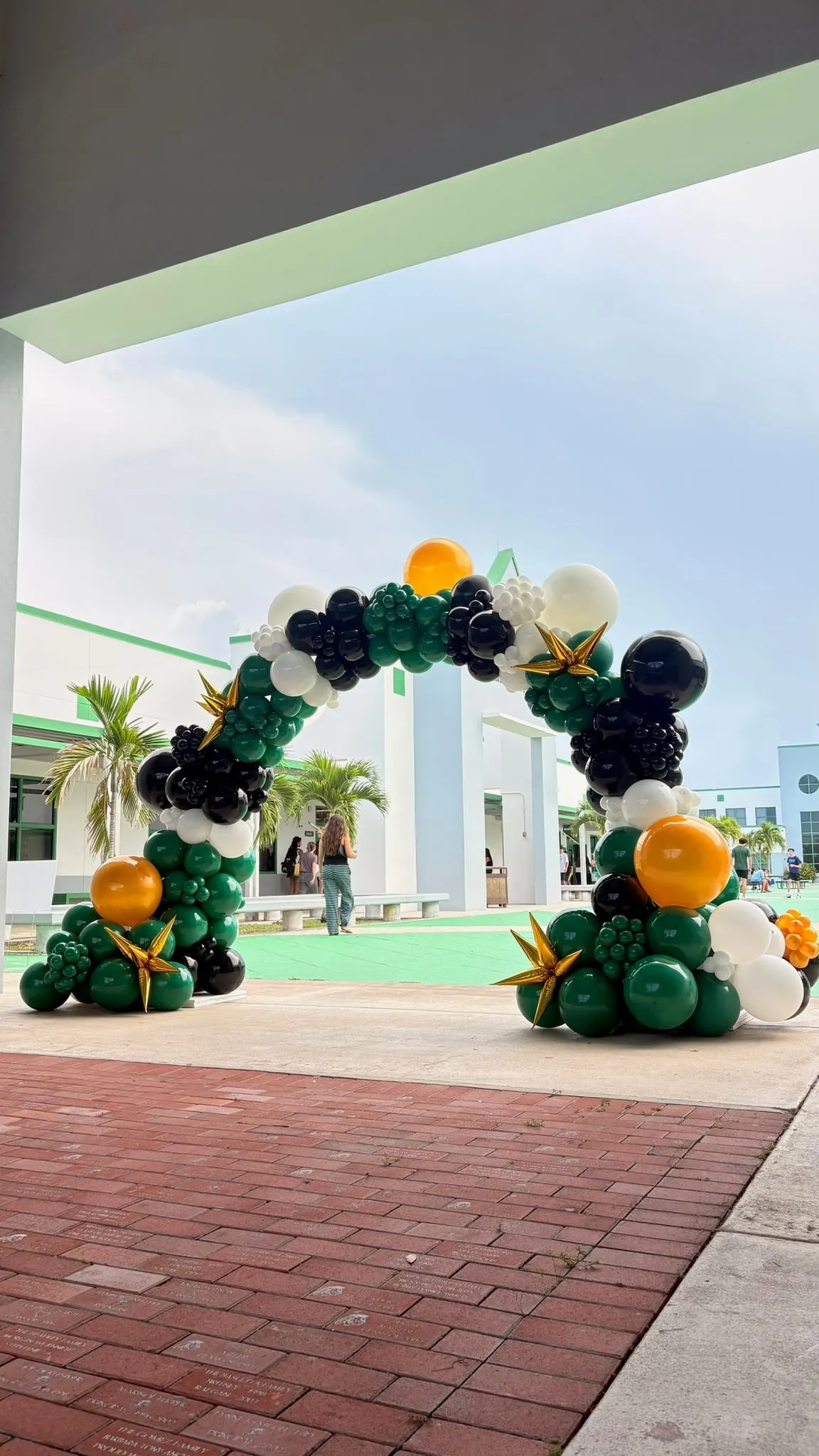 Outdoor balloon arch in green, black, white and gold at a school entrance