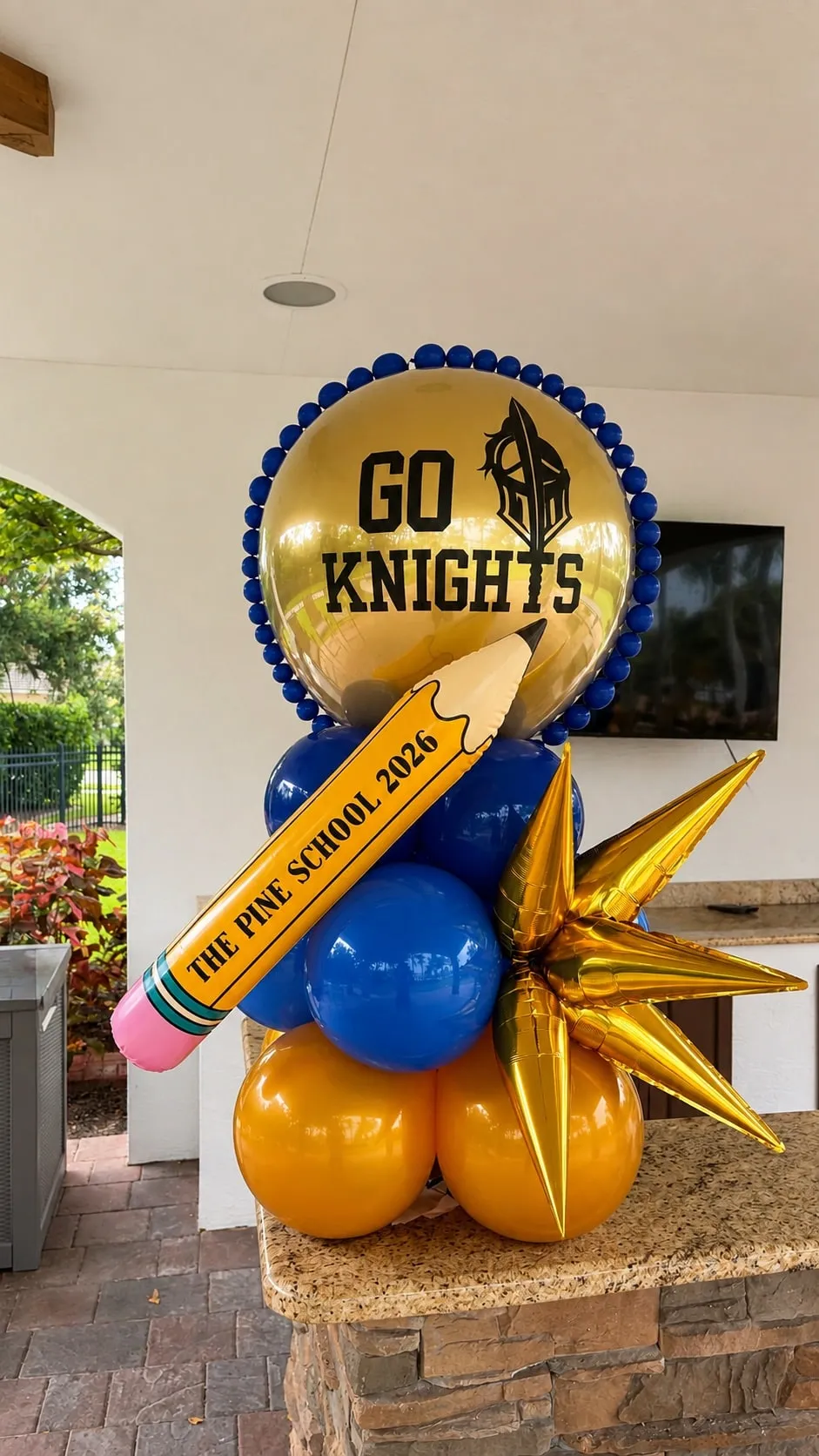 Balloon column with a gold printed topper, blue and gold balloons, a pencil balloon and a gold starburst