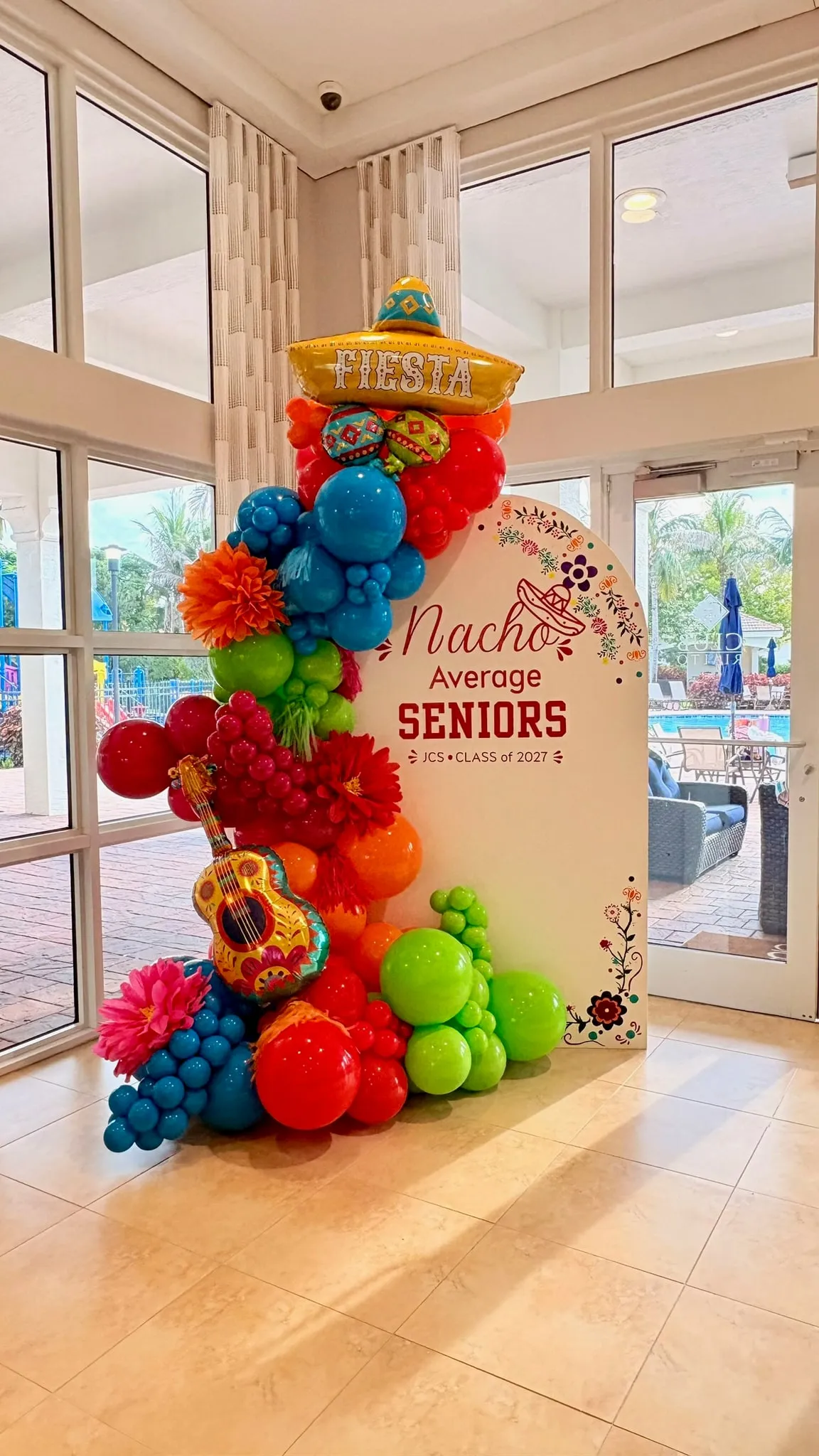 Bright balloon garland with a sombrero and guitar balloon beside an arched senior class backdrop