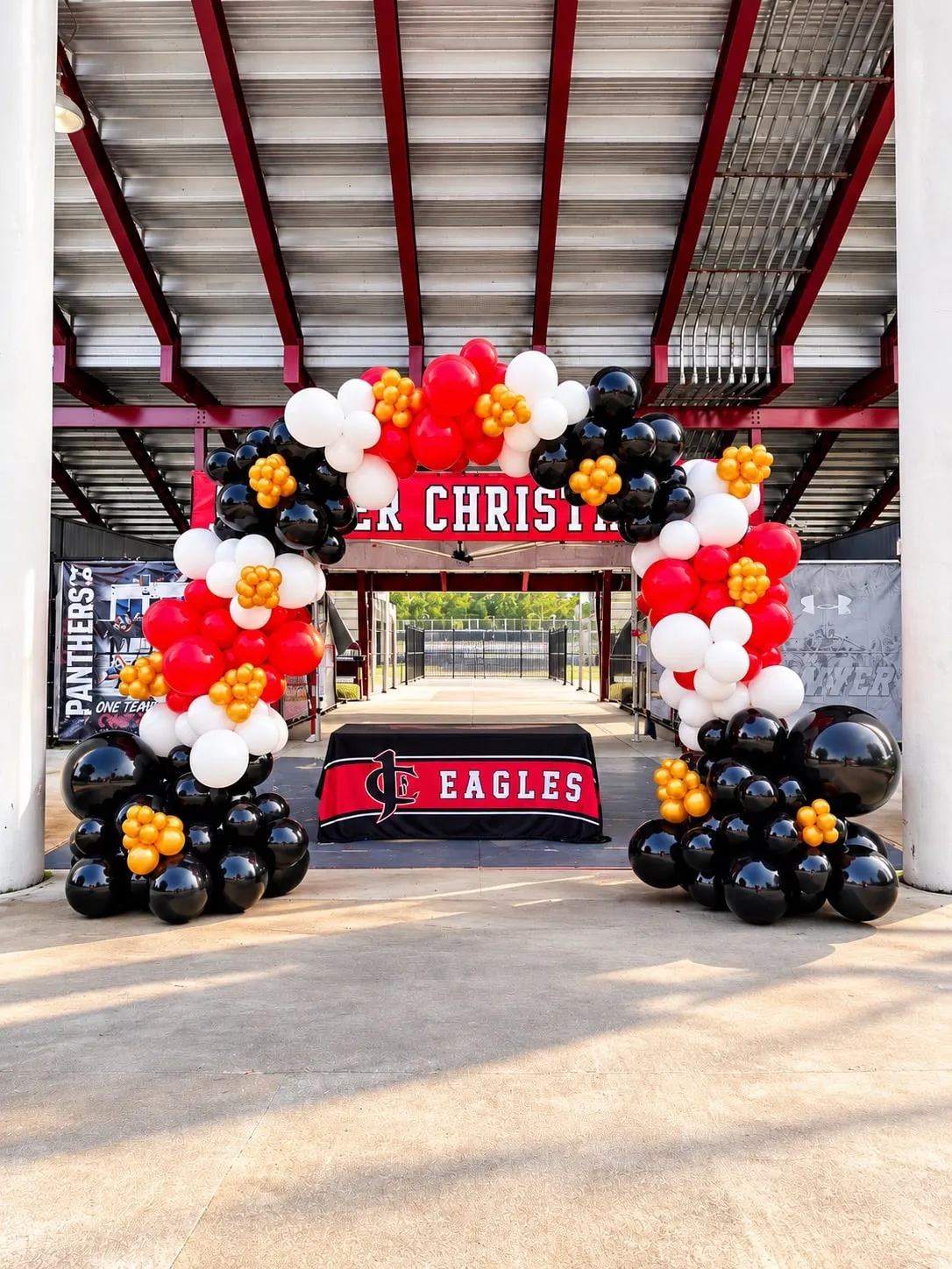 Red, white and black balloon arch with gold clusters at a stadium entrance