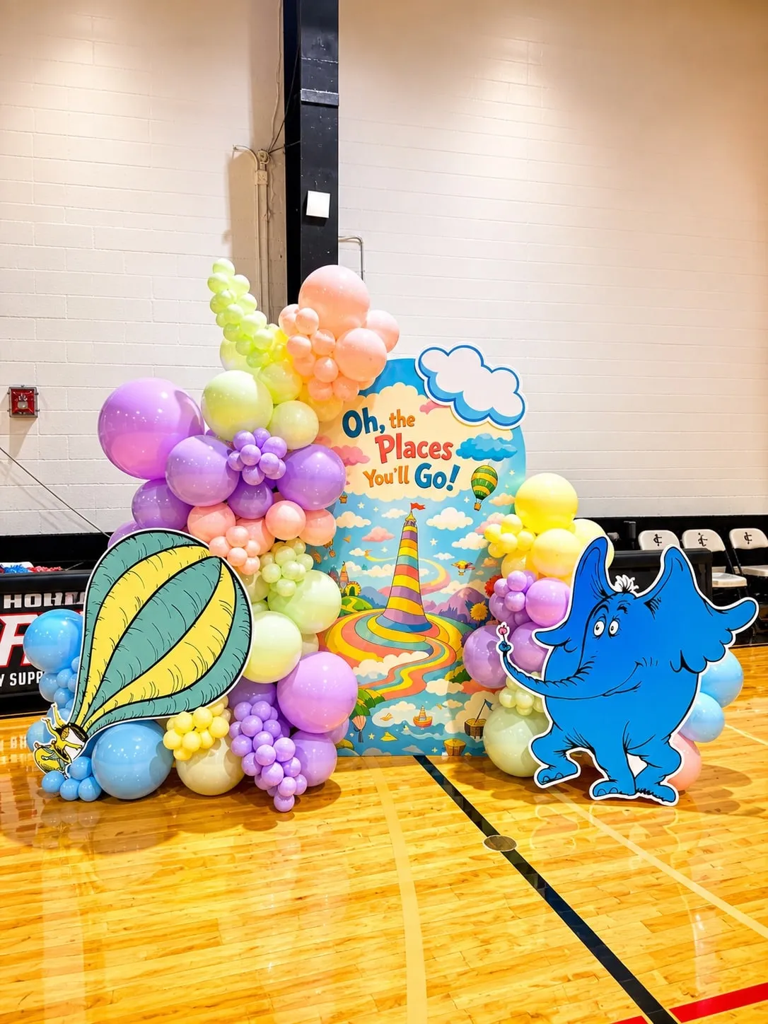 Pastel balloon garland around a storybook backdrop with a hot air balloon and character cutouts in a gym