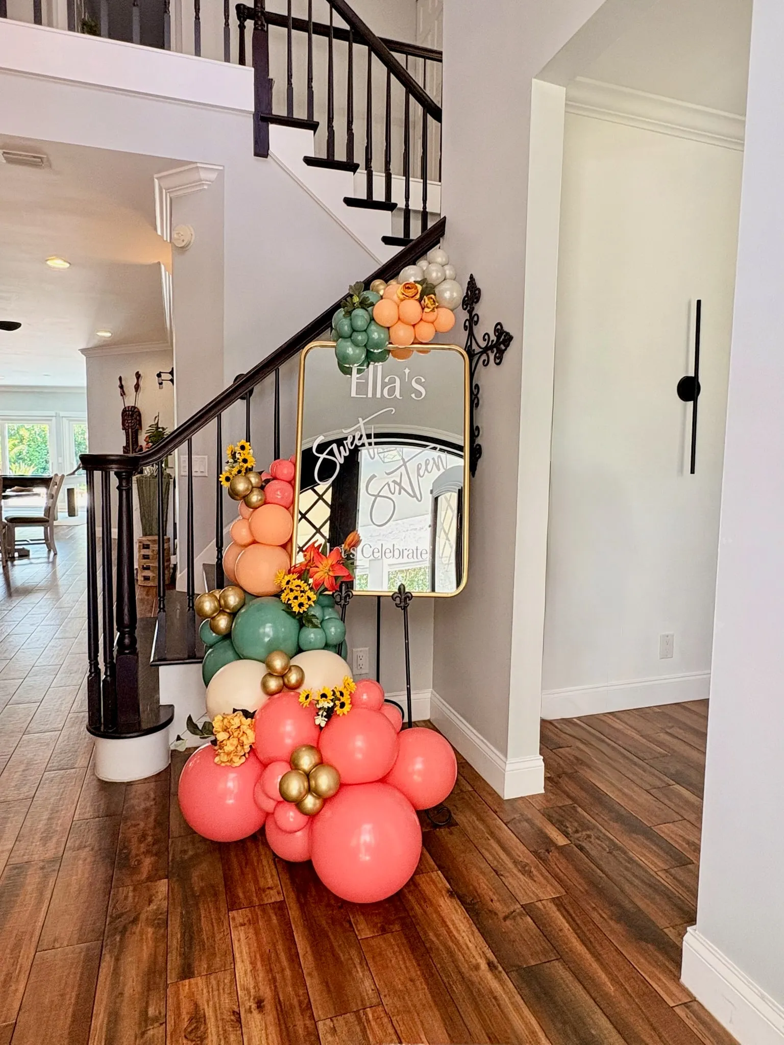 Mirrored welcome sign beside a staircase, dressed with coral, peach and sage balloons and sunflowers