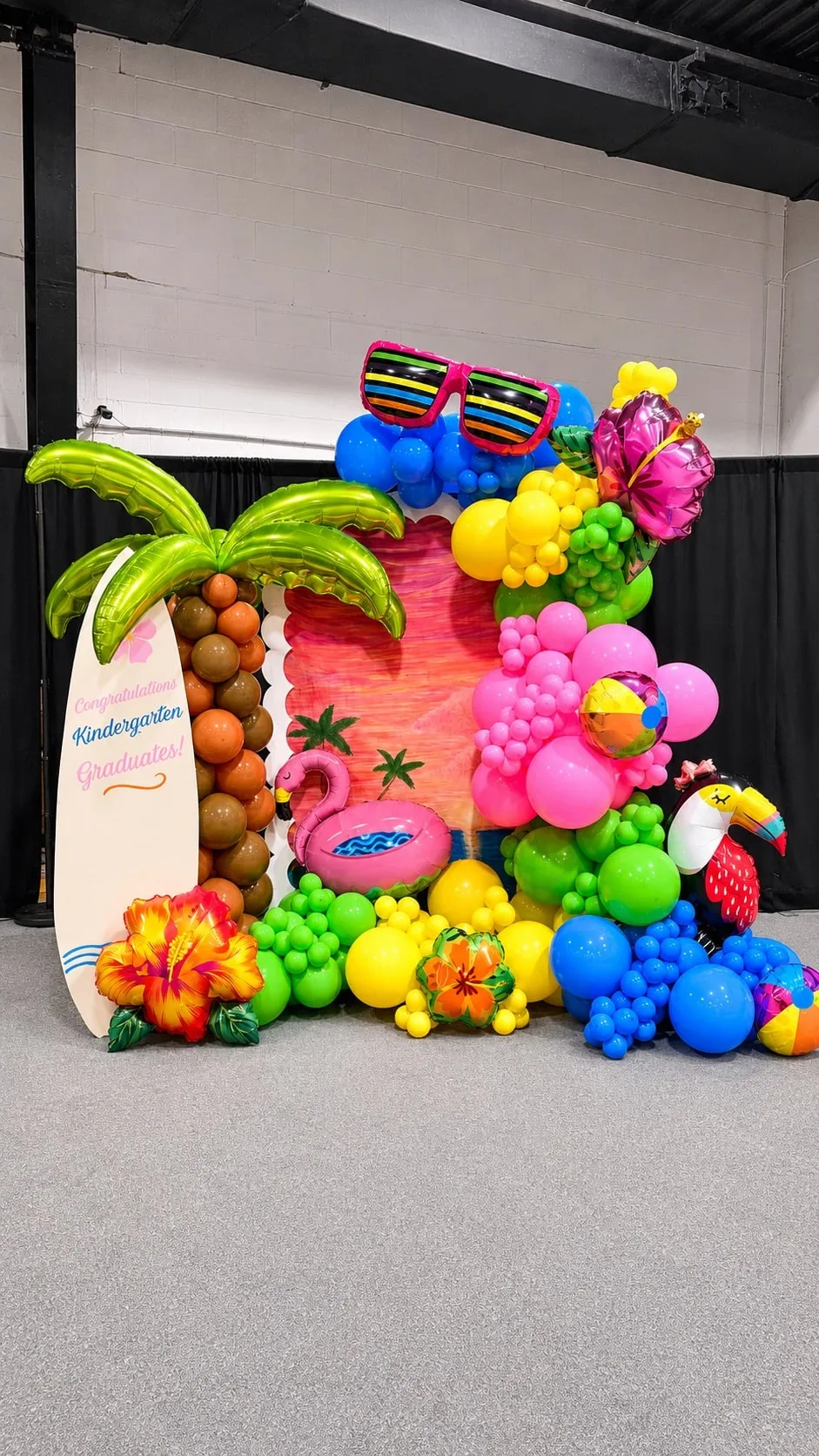 Close view of a tropical balloon backdrop with a palm tree, surfboard, flamingo float and toucan