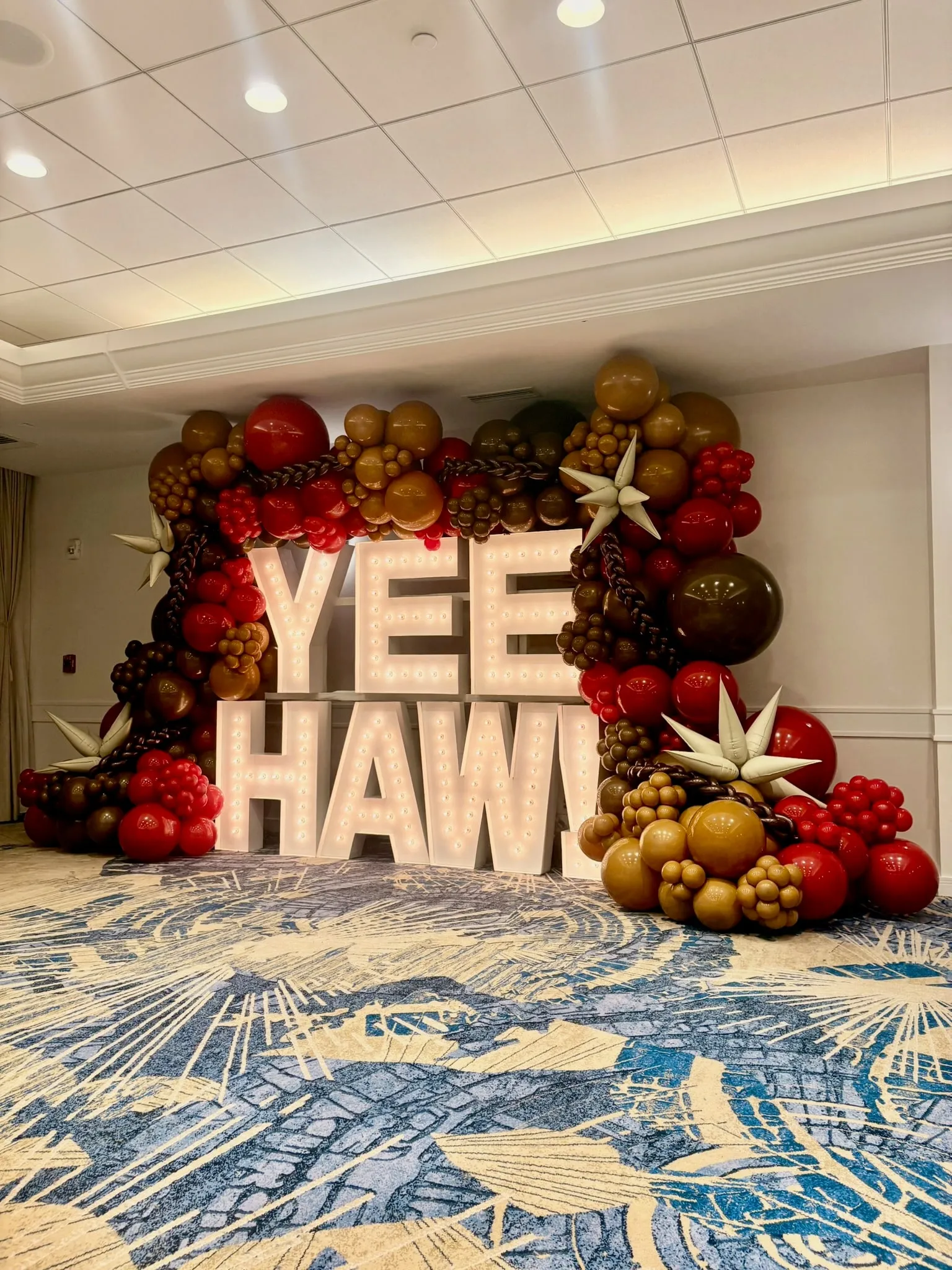 Light-up marquee letters framed by brown, red and caramel balloon garlands with star accents